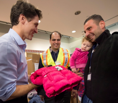 Justin Trudeau handiing out a coat tp Syrians